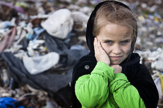 A beggar little girl in rags in a city dump close up