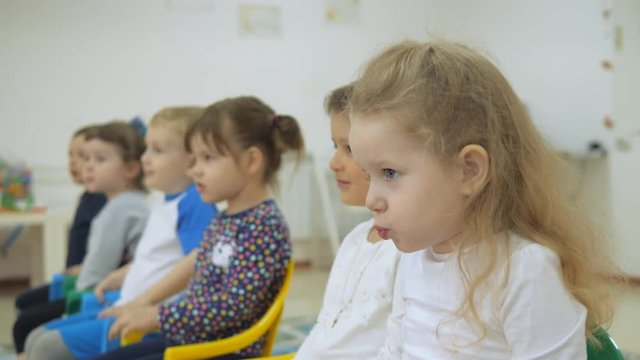 Children's developing a game room. Emotions of young children during entertaining classes. Children sit on chairs in a row. The child is building a cheerful expression. Grimaces and smeyotsya fun.