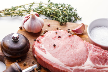 Raw pork steak, a bunch of fresh thyme, garlic, pepper and pepper mill, salt on a wooden cutting...