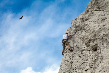 Man climbs to the top of the mountain. Rocks and blue sky. Bird in the sky and climbing wall.. To...
