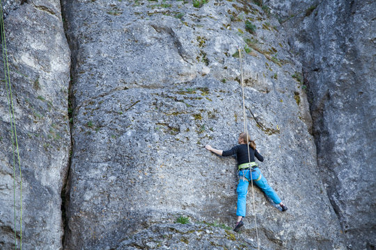 The woman climbs to the top of the mountain. A young girl on a climbing wall under the open sky. Climbing the rope and climb the mountain.