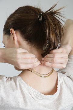 Woman putting gold necklace, back close up view
