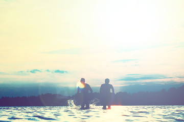 Glückliche junge Menschen laufen und springen am See beim Sonnenuntergang