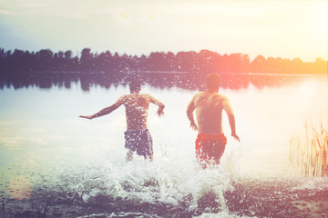 Glückliche junge Menschen laufen und springen am See beim Sonnenuntergang