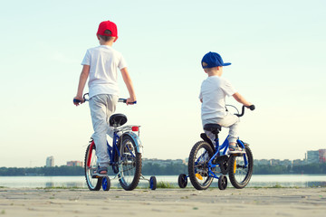 Two brothers rides a bicycle on the waterfront.