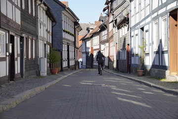 Fototapeta premium Woman driving a bicycle on a street with old nordic style houses in the town of Goslar, Germany in the Harz region.