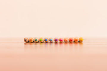 Front perspective of a row of twelve color pencils aligned on brown and white background
