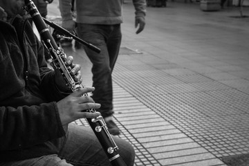 Hands of young man playing clarinet on street as pedestrian passes by in La Serena city, Chile....