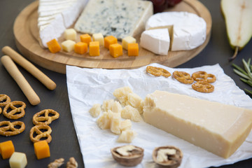 Tasting cheese plate with fruits, pretzels walnuts and bread sticks on dark background. Food for wine, romantic. Closeup.