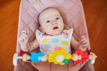 Baby girl sitting in bouncer and playing with colorful toys
