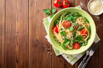 Spaghetti pasta with green beans, peas, cherry tomatoes, parsley and parmesan cheese on wooden table