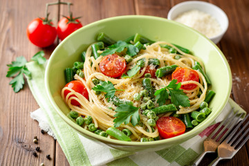 Spaghetti pasta with green beans, peas, cherry tomatoes, parsley and parmesan cheese on wooden table
