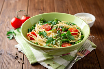 Spaghetti pasta with green beans, peas, cherry tomatoes, parsley and parmesan cheese on wooden table