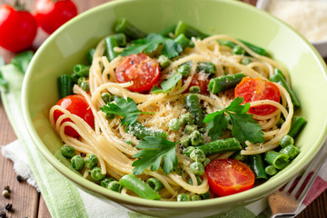 Spaghetti pasta with green beans, peas, cherry tomatoes, parsley and parmesan cheese on wooden table