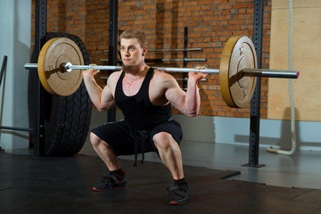 Fototapeta na wymiar a handsome young man with a beard is engaged in squatting with a barbell in the hall of a cross