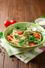Spaghetti pasta with green beans, peas, cherry tomatoes, parsley and parmesan cheese on wooden table