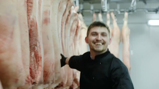crazy butcher smiling looking at camera running and touching pigs hanging on hooks in the slaughterhouse meat factory worker cheerful happy man madman fun joyful food business butchershop farmer