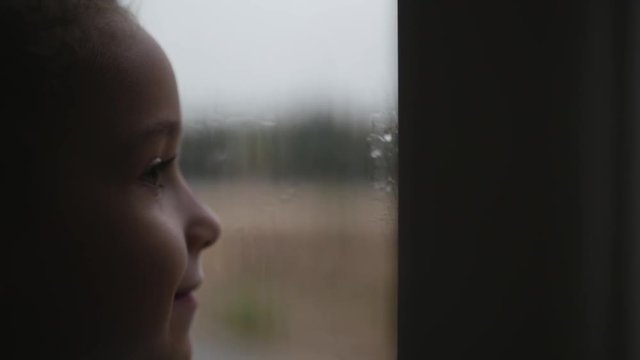 Little girl looks at the rain behind the window. Stock Footage.