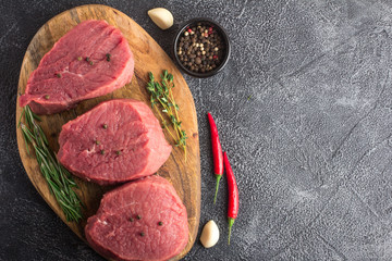 Raw beef meat with rosemary, thyme and chili pepper on a cutting board. Stone background. Copy space. Top flat view