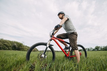 Low angle view of young man riding bicycle on a meadow with high green grass. Environmentally friendly transport, clean air, activity, healthy lifestyle concept