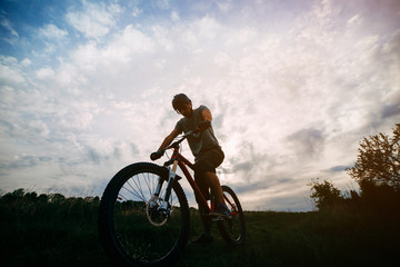 Obraz premium Bicycle sports, traveling, healthy lifestyle and activity. Silhouette of young man riding bicycle along a country road in sunset light