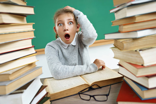 Schoolgirl is shocked. Photo of little girl with an open mouth and big eyes around books. The concept of education