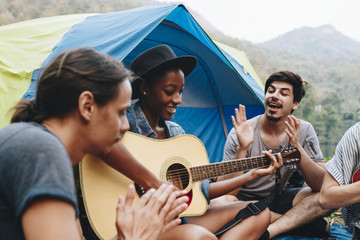 Group of young adult friends in camp site playing guitar and ukelele and singing together outdoors recreational leisure and friendship concept