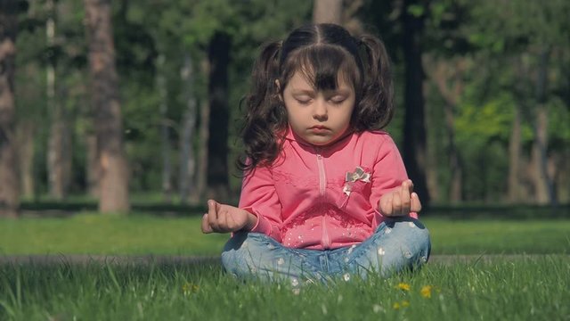 The child is engaged in yoga. A girl in a lotus pose in a park.