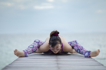 beautiful woman playing yoga in turtle pose on sea wooden pier