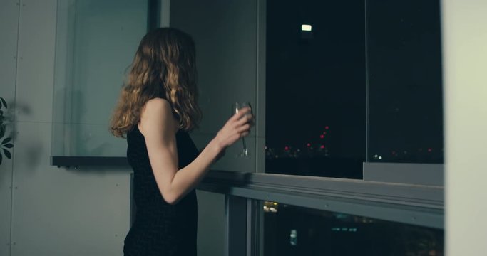 Elegant woman in dress drinking wine on city balcony