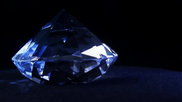 Video of a shining and glowing luxury blue toned diamond laying on a cloth black showcase background and rolling counterclock-wise.
