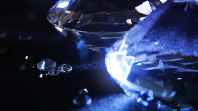 Video of a shining and glowing luxury blue toned diamonds with small stones laying on a cloth black showcase background and rolling counterclock-wise.