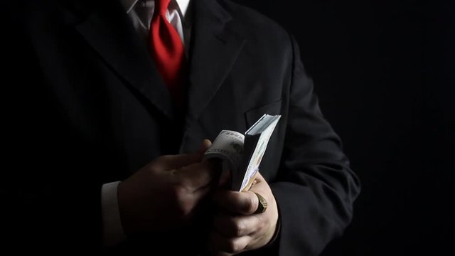 Photo of a rich businessman in black siut with red tie holding and counting money pack.