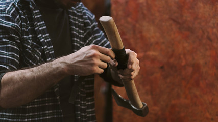 Man working in carpentry workshop. He wraps wooden handle of ax with leatherwork material. Men at work. Hand work.