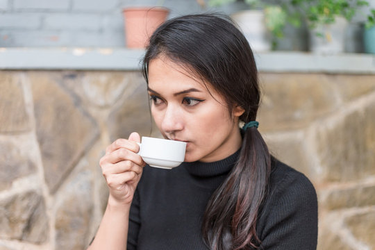 Asian woman holding white cup and drinking a hot coffee or tea in cafe.