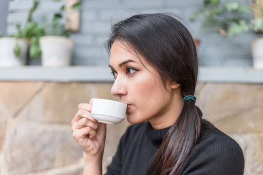 Asian woman holding white cup and drinking a hot coffee or tea in cafe.