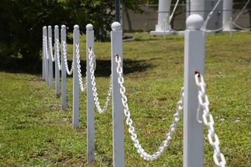 Droops of White Chain Links comprising Strands of a Barricaded Fence against Green Grass Next to...