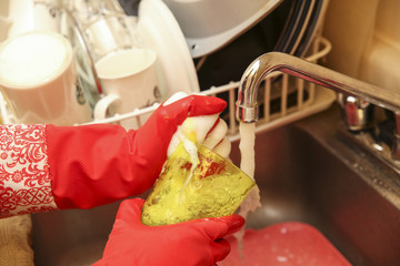 Detail of hands using rubber gloves to wash a yellow glass