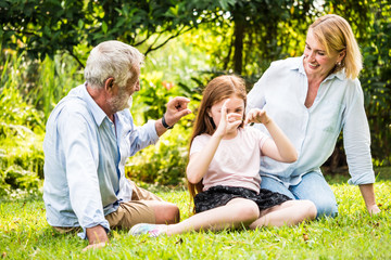 Fototapeta premium Szczęśliwa rodzina wspólnej zabawy w ogrodzie. Ojciec, matka i córka siedzą na trawie w parku.