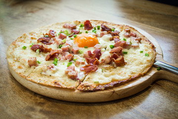 Gourmet pizza with egg and bacon on rustic wooden background and room for copy space.