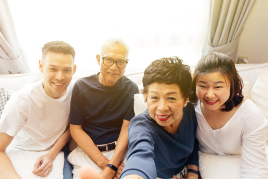 Asian family with adult children and senior parents taking selfie and sitting on a sofa at home. Happy and relaxing family time