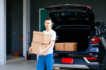 Mature Asian man carrying cardboard boxes from car trunk at new home