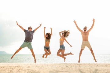 Happy young energetic group of friends jumping at the beach in summer