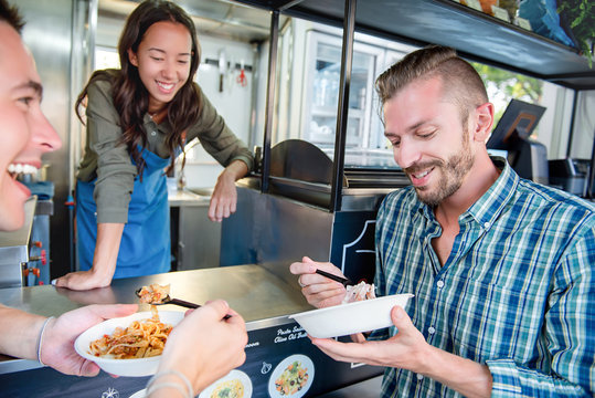 People enjoy eating pasta at counter of food truck