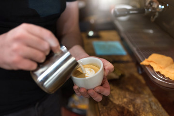 baristas pours milk in coffee cup