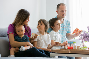Beautiful young family with three children, eating pizza at home and watching TV