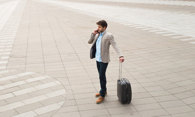 Strategic thinking! Handsome young businessman with his luggage standing and talking on phone at the airport, while waiting for his departure.