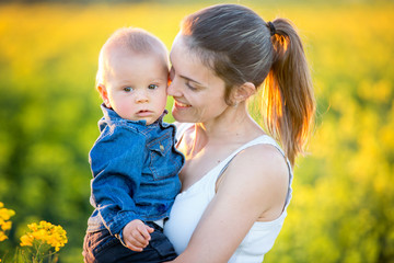 Young mother holding up her todller son in canola field