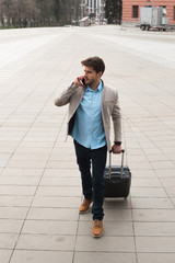 Going only forward! Smart serious travelling businessman with a suitcase making phone call and going to the business trip abroad.