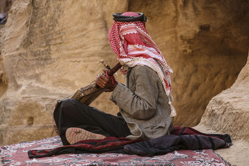Old bedouin in the keffiyeh plays on the national musical instrument of Jordan,Petra, Jordan